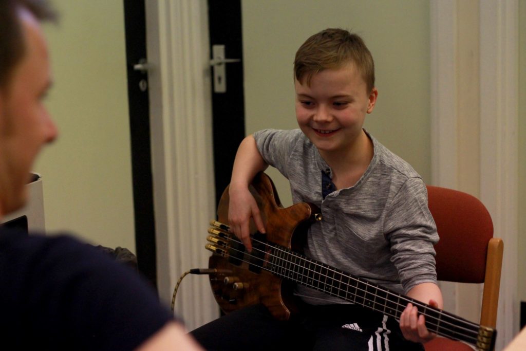 Young person smiling, sitting and holding electric bass guitar