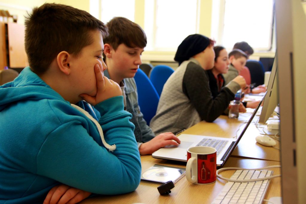 Group of young people sitting in office chairs in a computer lab, looking thoughtful and hard at work