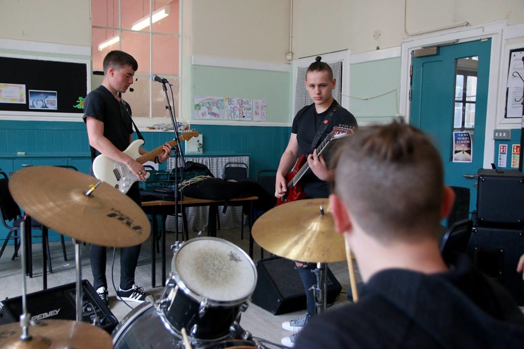Young three-piece band with guitar, bass and drum kit practising in a rehearsal space.